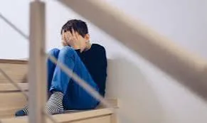 A child sitting alone on the stairs with their head in their hands, looking overwhelmed and self-critical